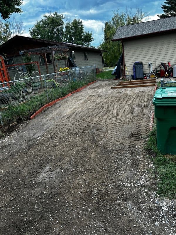 Gravel driveway preparation with surrounding houses and greenery in the background.