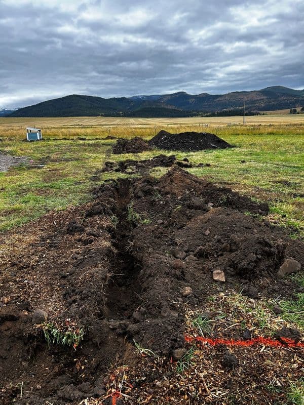 Excavation site with trenches and mounds of soil against a scenic mountainous background.