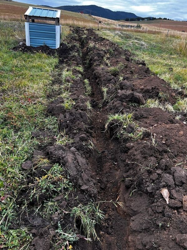Trenched field with freshly turned soil and a small shed in a scenic rural landscape.