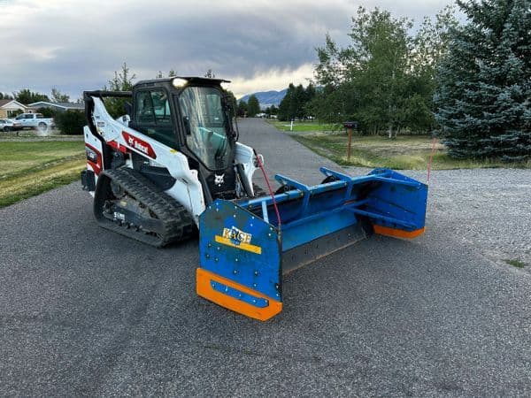 Bobcat skid steer loader with snow plow attachment on a residential street at sunset.