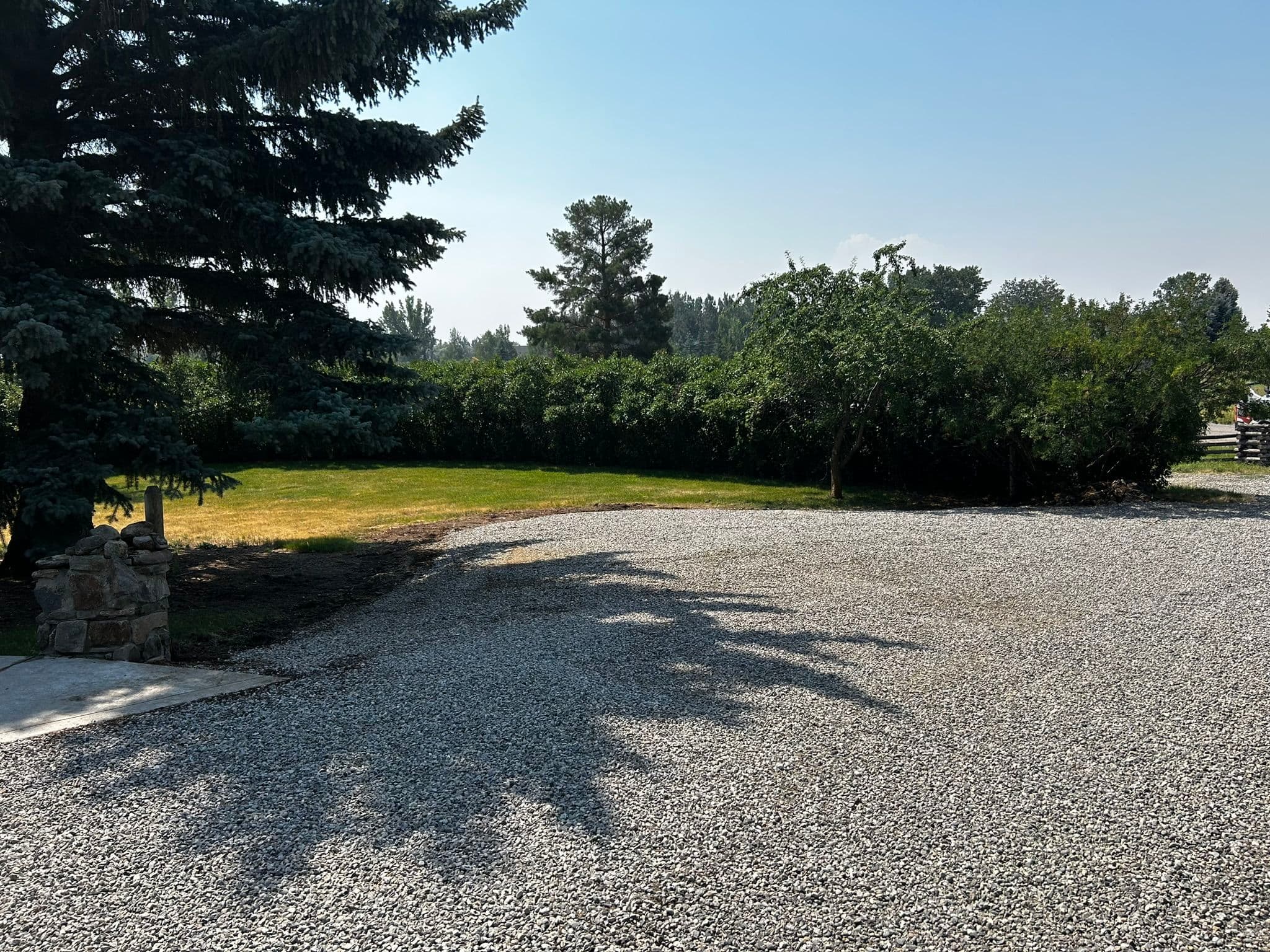 Gravel driveway with greenery and trees under a clear blue sky.